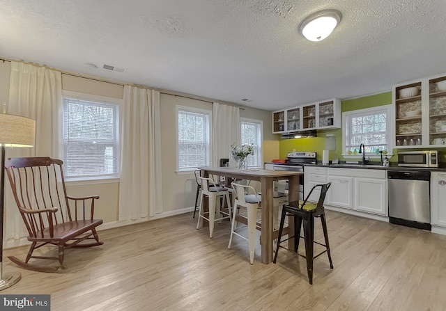 kitchen with sink, light hardwood / wood-style flooring, stainless steel appliances, a textured ceiling, and white cabinets