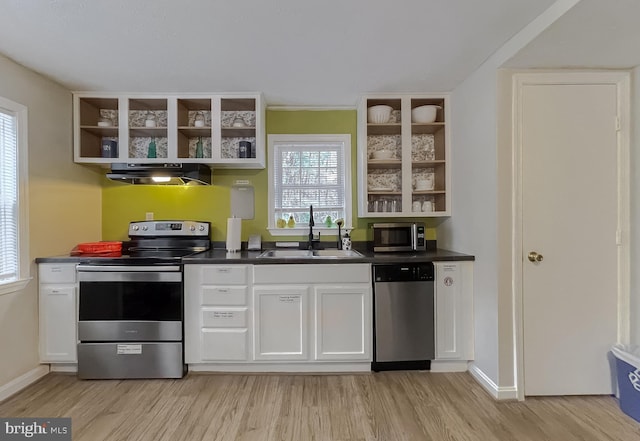 kitchen with appliances with stainless steel finishes, range hood, white cabinetry, sink, and light hardwood / wood-style flooring