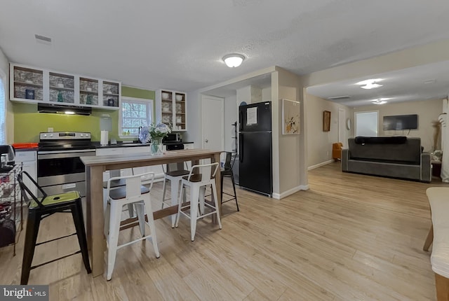 kitchen featuring black refrigerator, stainless steel range with electric stovetop, light hardwood / wood-style floors, a textured ceiling, and a kitchen bar