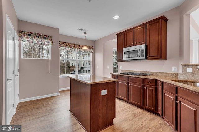 kitchen with light stone countertops, visible vents, appliances with stainless steel finishes, a center island, and light wood finished floors