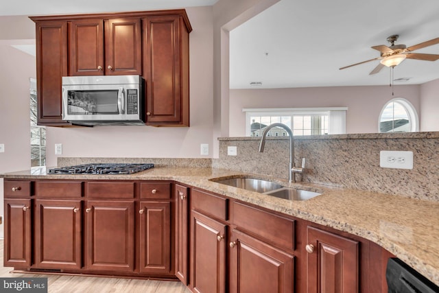 kitchen featuring a ceiling fan, appliances with stainless steel finishes, light stone counters, light wood-style floors, and a sink