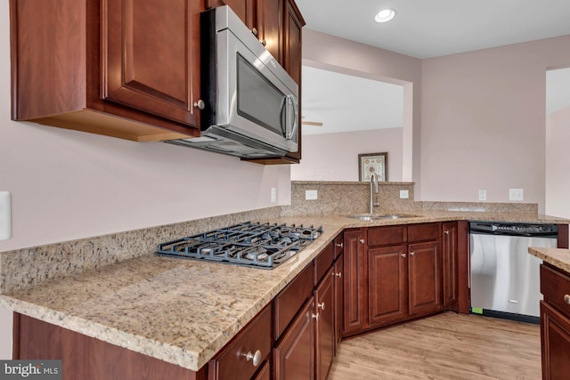 kitchen featuring stainless steel appliances, light wood finished floors, a sink, and light stone countertops