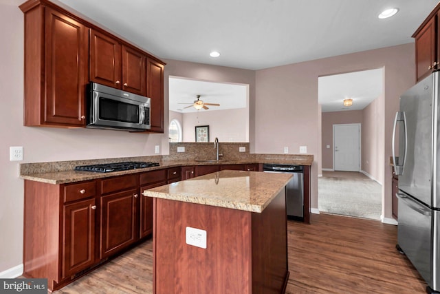 kitchen with dark wood finished floors, light stone counters, appliances with stainless steel finishes, a center island, and a sink