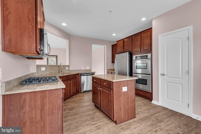 kitchen with appliances with stainless steel finishes, light wood-type flooring, a sink, and a center island