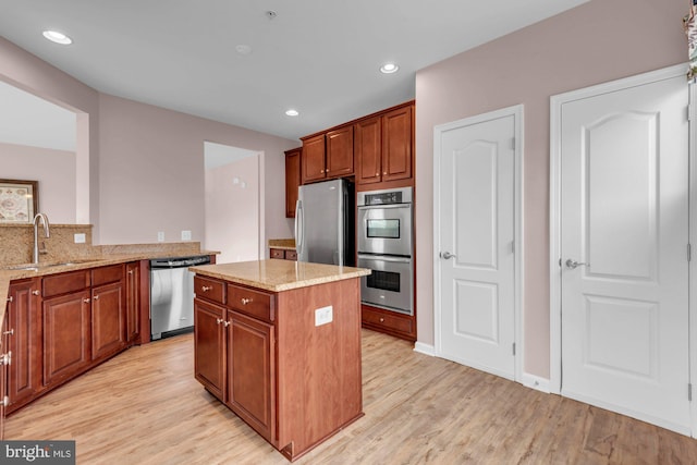 kitchen featuring light wood-type flooring, light stone countertops, appliances with stainless steel finishes, and a sink