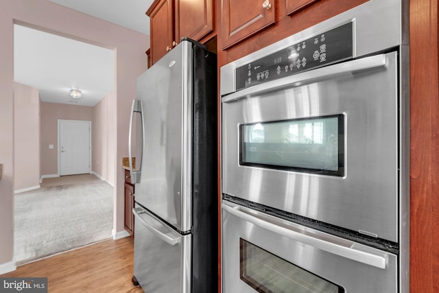 kitchen featuring stainless steel appliances, brown cabinets, light wood-style floors, and baseboards