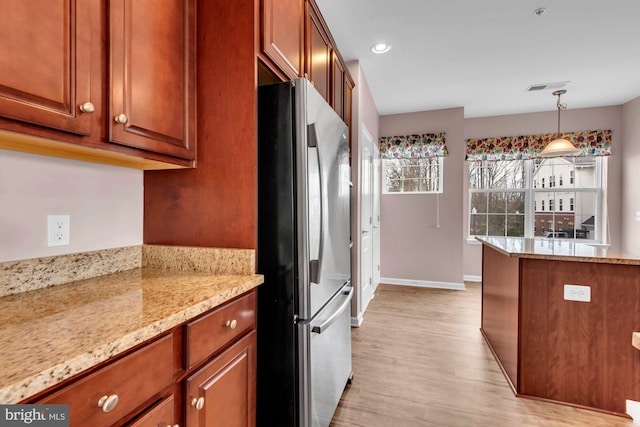 kitchen featuring baseboards, visible vents, freestanding refrigerator, hanging light fixtures, and light wood-type flooring