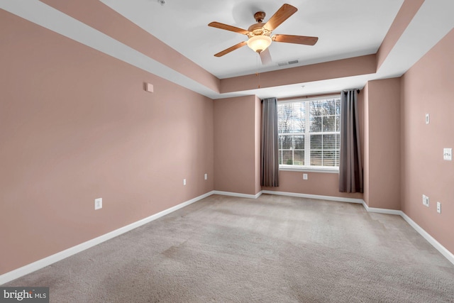 carpeted empty room featuring a ceiling fan, a raised ceiling, visible vents, and baseboards