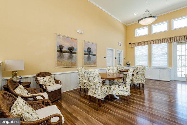 dining space featuring a high ceiling, ornamental molding, wood finished floors, and wainscoting