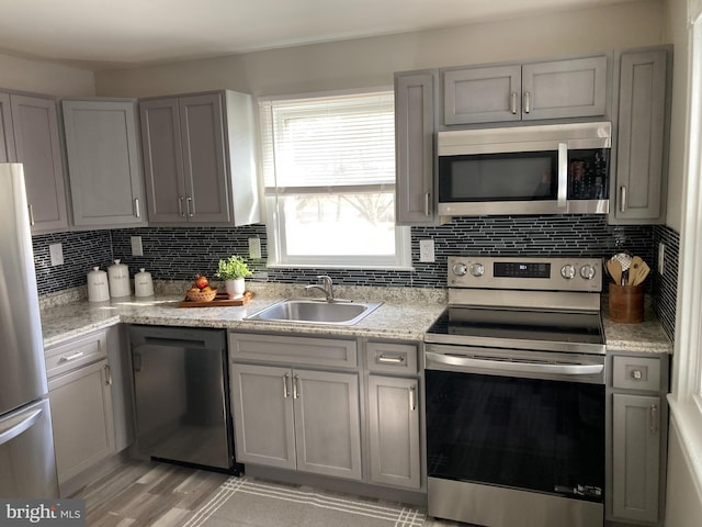 kitchen with appliances with stainless steel finishes, backsplash, a sink, and gray cabinetry