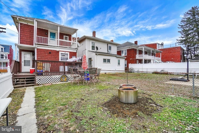 rear view of house featuring a wooden deck, a lawn, and a balcony