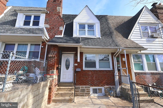 view of front facade featuring entry steps, brick siding, roof with shingles, and fence