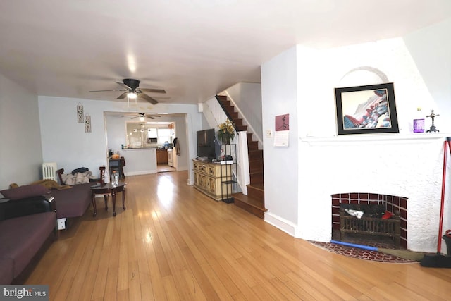 living room with a ceiling fan, a tiled fireplace, radiator heating unit, light wood-style flooring, and stairway