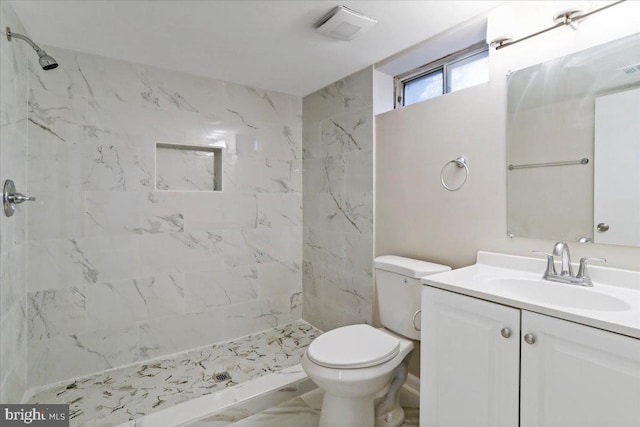 bathroom featuring vanity, a tile shower, and toilet