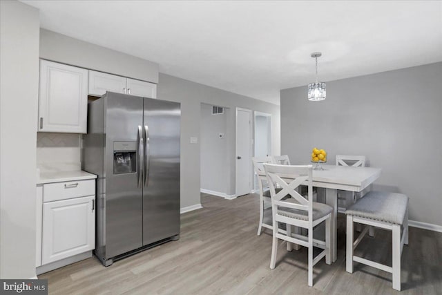 kitchen with white cabinetry, stainless steel refrigerator with ice dispenser, pendant lighting, and light hardwood / wood-style flooring