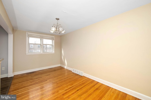 spare room with a notable chandelier and light wood-type flooring