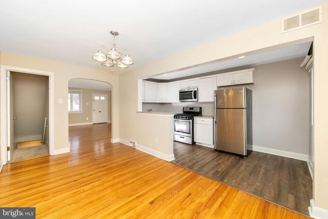 kitchen with an inviting chandelier, appliances with stainless steel finishes, white cabinetry, and decorative light fixtures