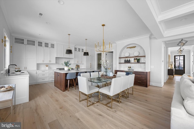 dining space featuring crown molding, a chandelier, sink, and light hardwood / wood-style flooring