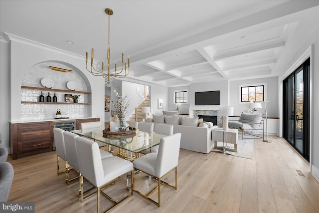 dining area with bar, beam ceiling, coffered ceiling, a chandelier, and light wood-type flooring