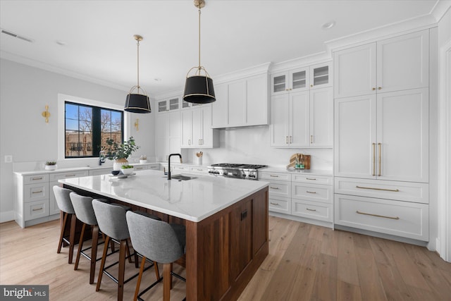 kitchen with pendant lighting, white cabinetry, sink, light stone countertops, and a center island with sink