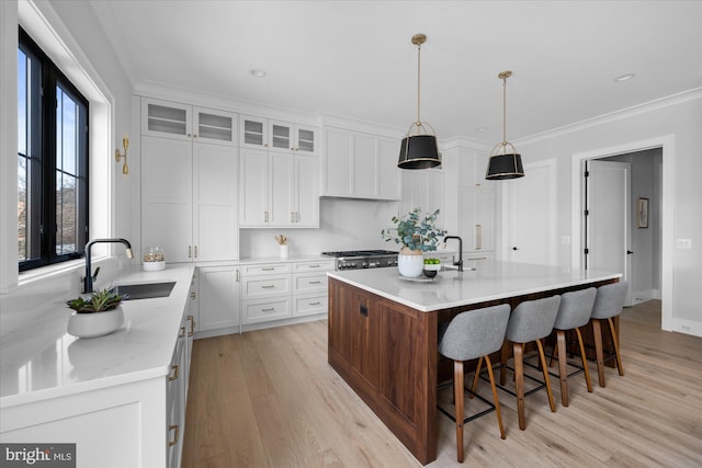 kitchen featuring sink, ornamental molding, pendant lighting, a kitchen island with sink, and white cabinets