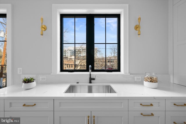 kitchen with white cabinetry, light stone countertops, and sink