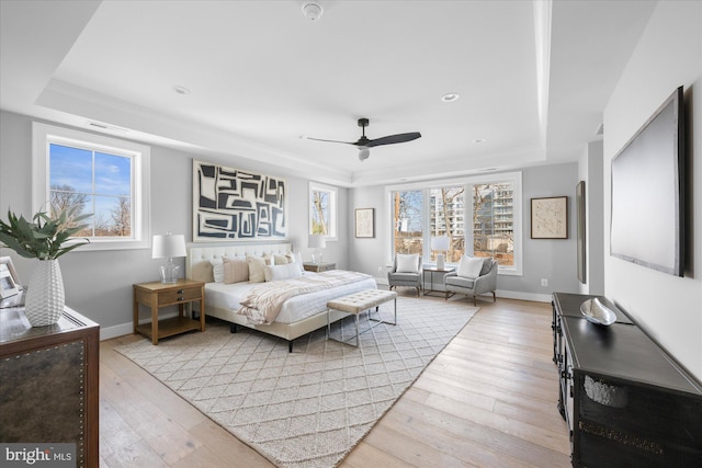 bedroom with a raised ceiling, ceiling fan, and light wood-type flooring