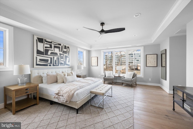 bedroom with ornamental molding, light hardwood / wood-style flooring, ceiling fan, and a tray ceiling