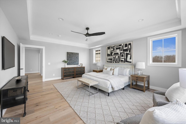 bedroom featuring ceiling fan, light hardwood / wood-style floors, and a tray ceiling