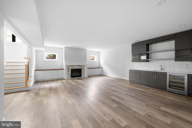 unfurnished living room with a premium fireplace, sink, beverage cooler, and light hardwood / wood-style flooring