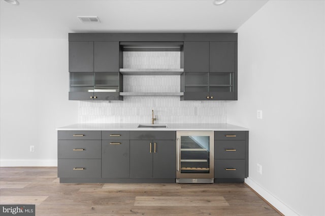 bar with tasteful backsplash, sink, gray cabinetry, beverage cooler, and light hardwood / wood-style flooring