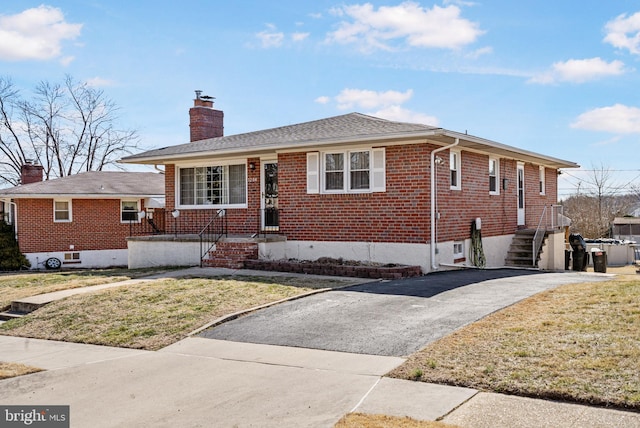 bungalow-style home featuring aphalt driveway, a chimney, a front lawn, and brick siding