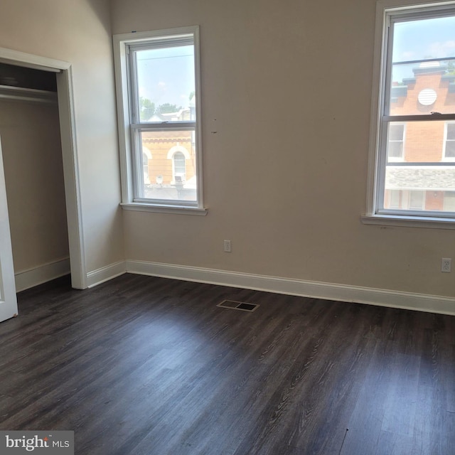 unfurnished bedroom with multiple windows, dark hardwood / wood-style flooring, and a closet