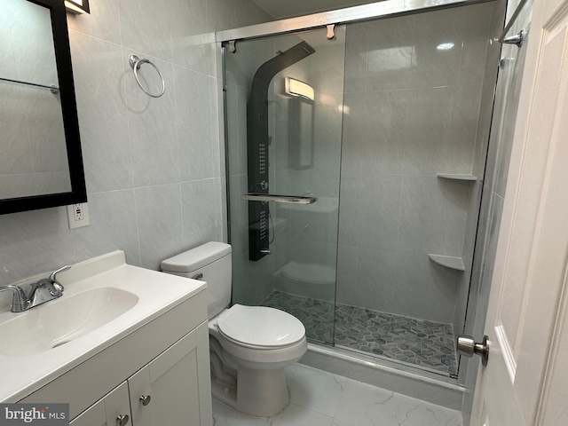 bathroom with a shower with door, vanity, tile walls, and toilet