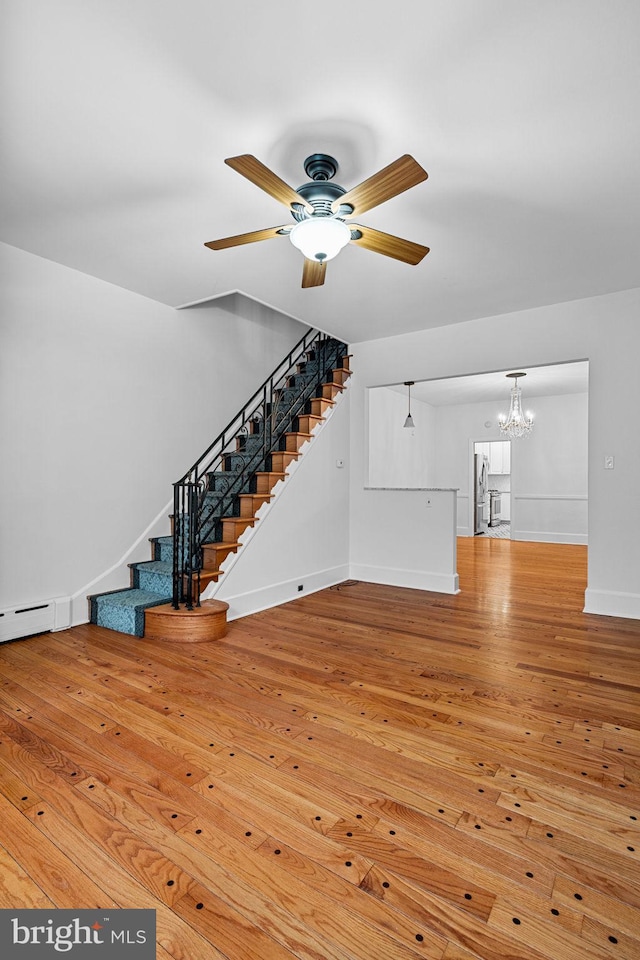 unfurnished living room featuring ceiling fan with notable chandelier and light hardwood / wood-style flooring