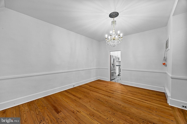 empty room featuring wood-type flooring and an inviting chandelier