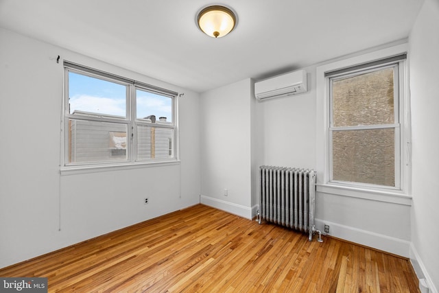 spare room featuring radiator, light hardwood / wood-style floors, and a wall unit AC