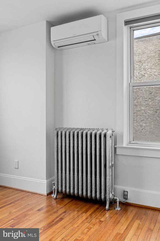 room details with radiator, hardwood / wood-style flooring, and an AC wall unit