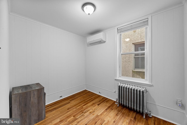 unfurnished room with radiator heating unit, hardwood / wood-style floors, and a wall mounted air conditioner