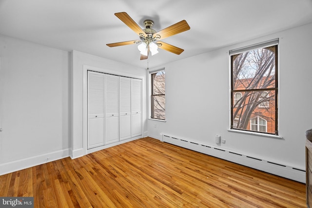 unfurnished bedroom featuring a baseboard radiator, ceiling fan, light hardwood / wood-style floors, and a closet