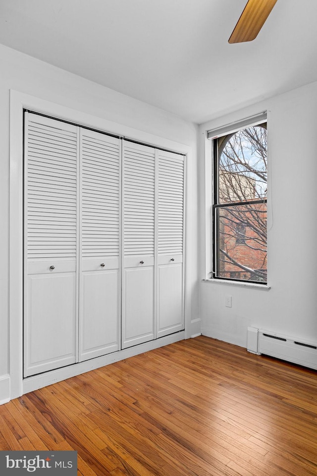 unfurnished bedroom with hardwood / wood-style flooring, baseboard heating, and a closet