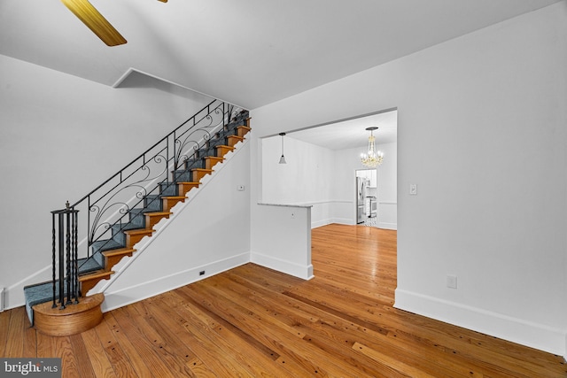 stairway with wood-type flooring and ceiling fan with notable chandelier