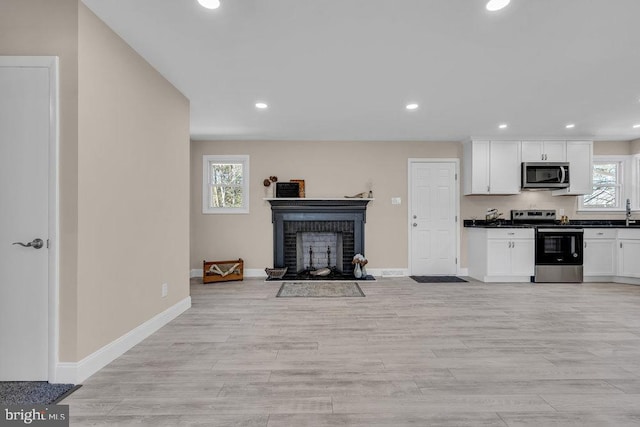 kitchen with light wood-style flooring, stainless steel appliances, white cabinetry, a brick fireplace, and dark countertops