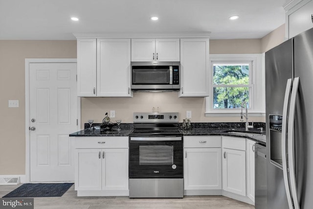 kitchen with visible vents, dark stone counters, appliances with stainless steel finishes, white cabinetry, and a sink