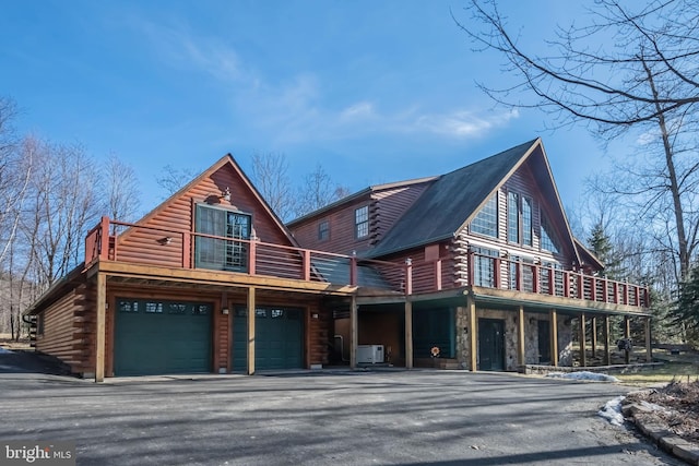 log-style house featuring log exterior, a wooden deck, driveway, stone siding, and an attached garage