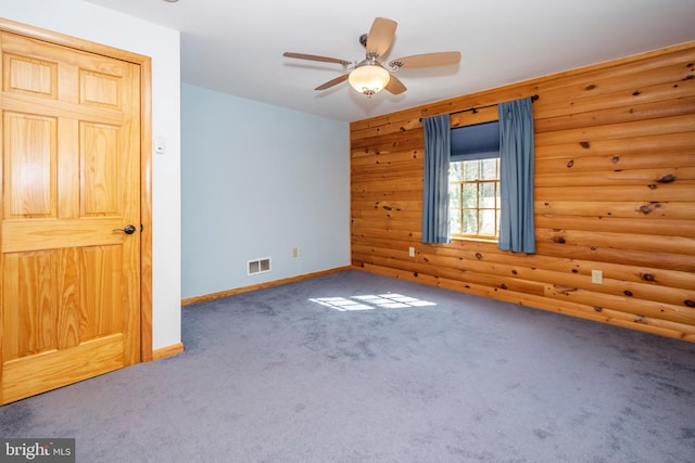 carpeted empty room featuring ceiling fan, baseboards, visible vents, and log walls