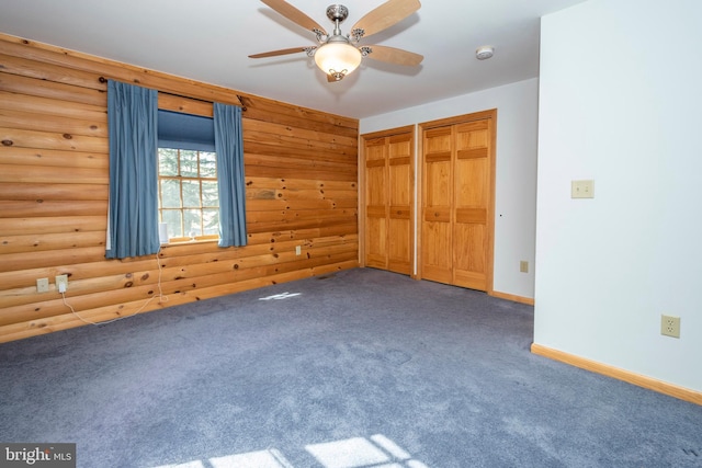 unfurnished bedroom with carpet, baseboards, log walls, ceiling fan, and two closets