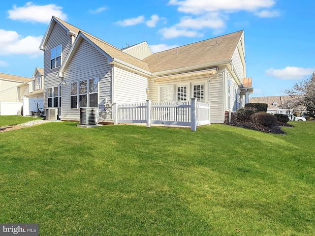 rear view of house featuring central air condition unit and a lawn