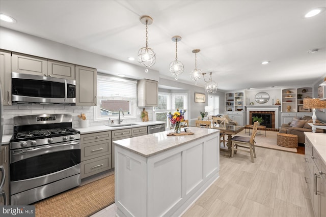 kitchen featuring gray cabinets, appliances with stainless steel finishes, a brick fireplace, open floor plan, and a sink