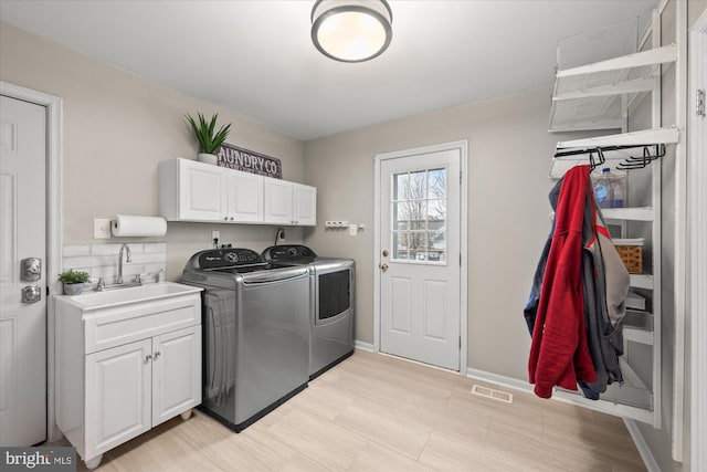 washroom featuring cabinet space, baseboards, visible vents, washer and dryer, and a sink